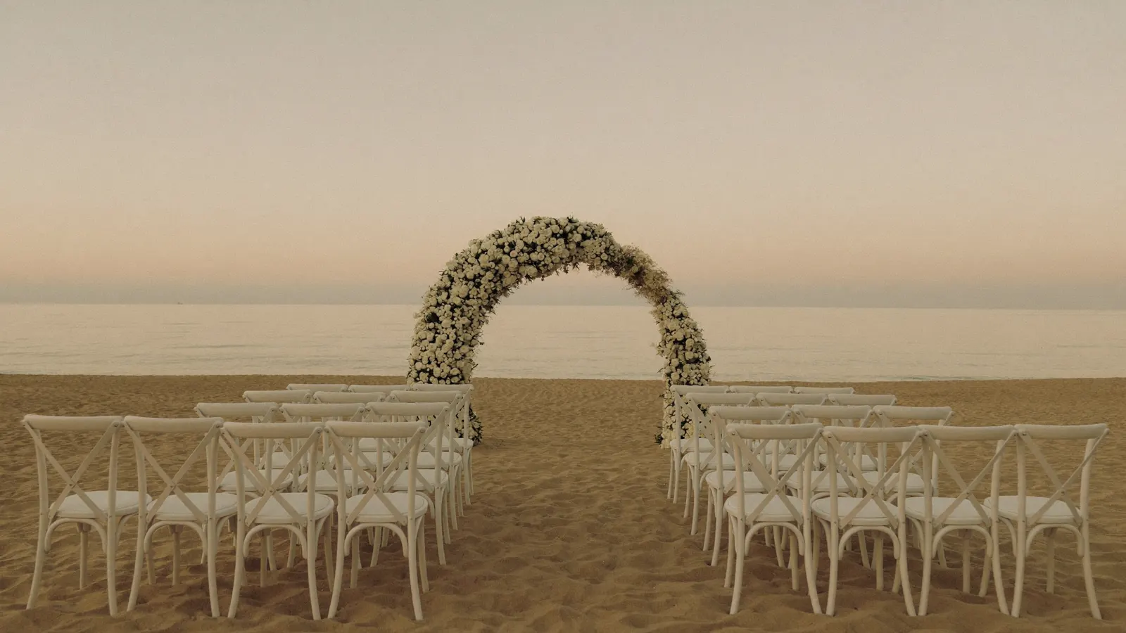 Cerimônia de casamento na praia ao pôr do sol com arco de flores